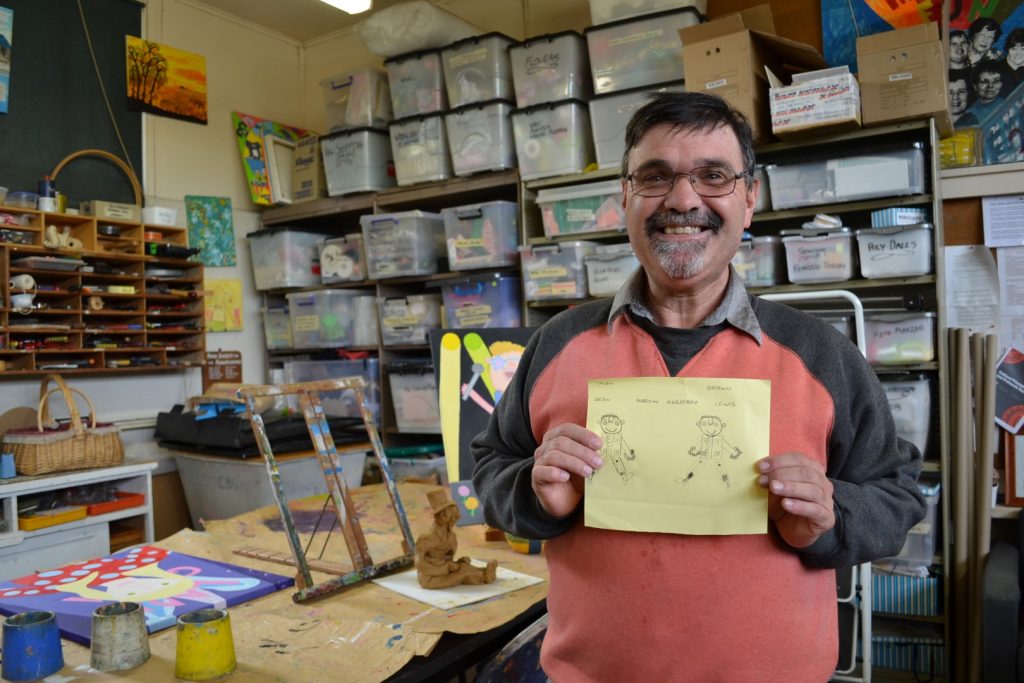 Orana client at an arts and crafts program, smiling and holding his drawing.