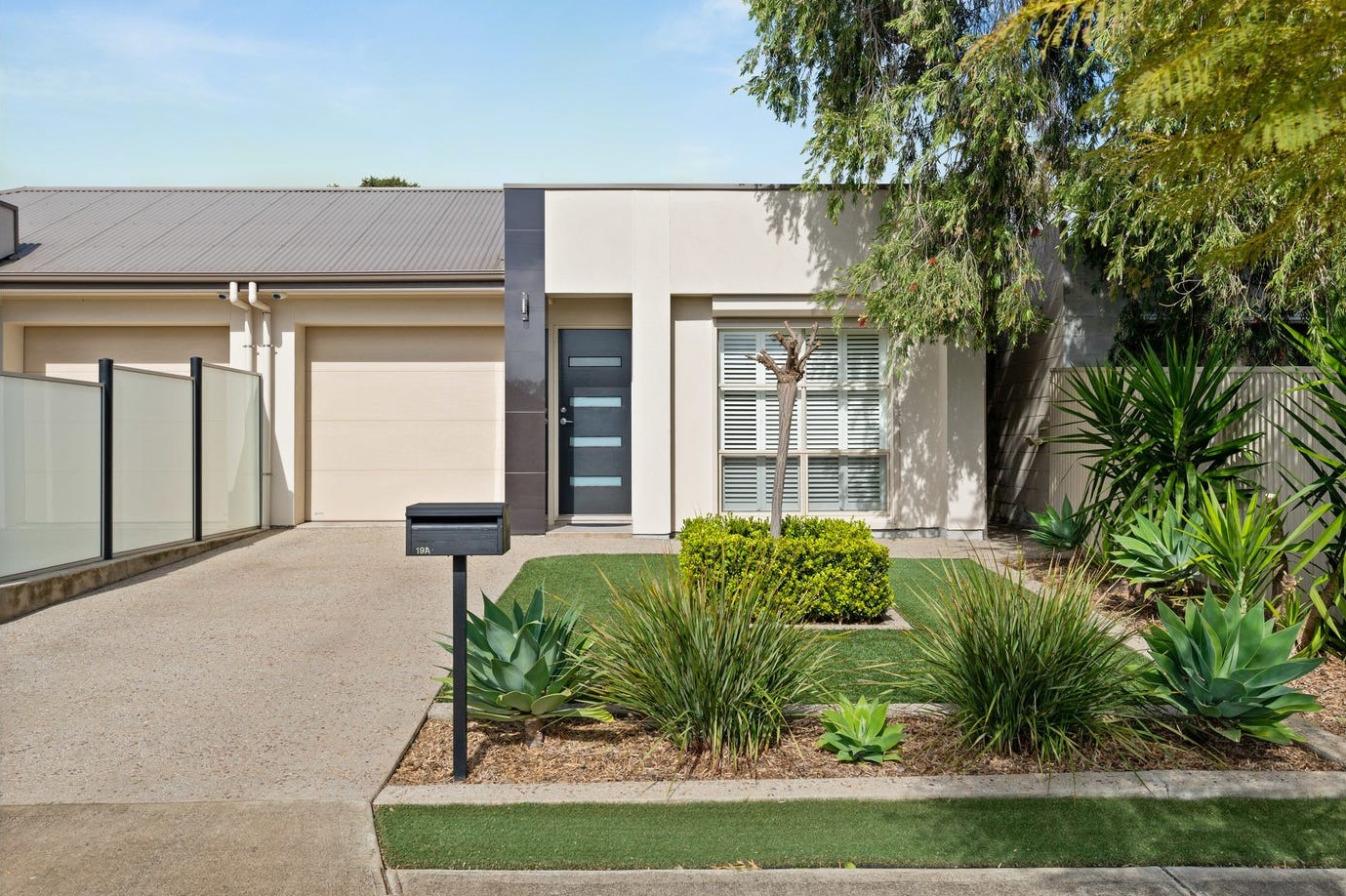 Facade of Clovelly park home. White panelling with black wooden door. Small front yard with low green bushes. 
