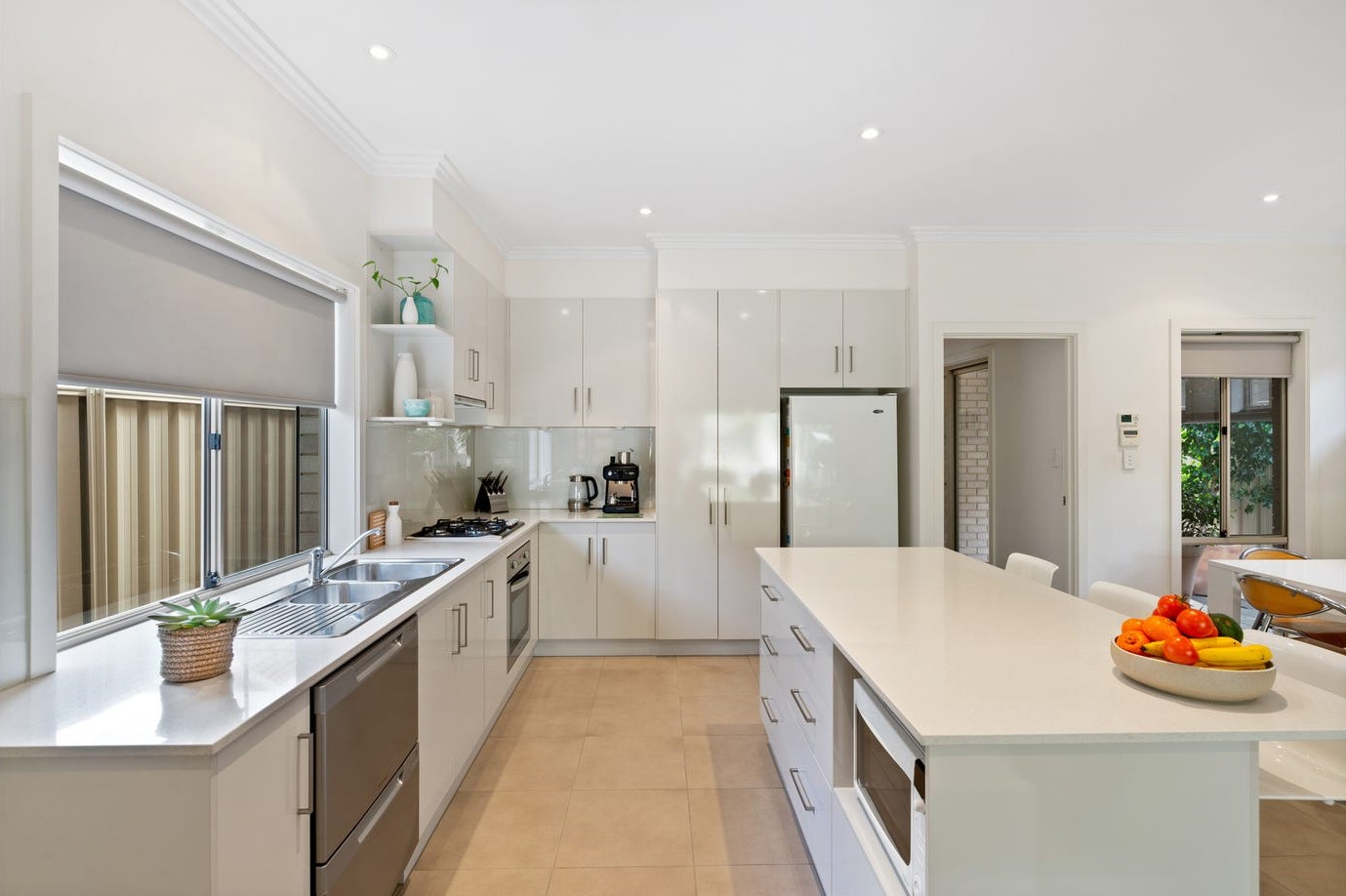 New modern kitchen with white cabinetry and white stone benchtops. A bowl of fruit is sitting on the edge of the bench. 