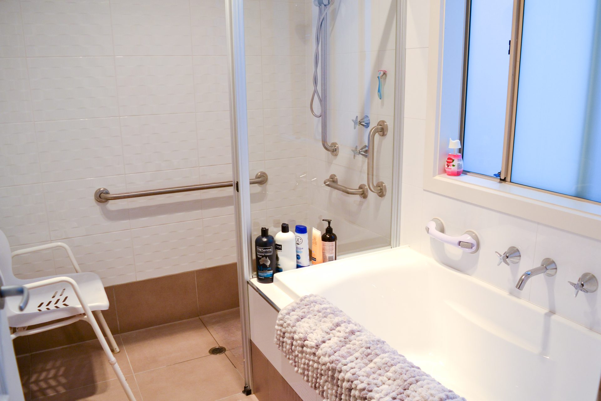 Bathroom with multiple safety rails in place. A plush bath mat sits across the top of the bath. 