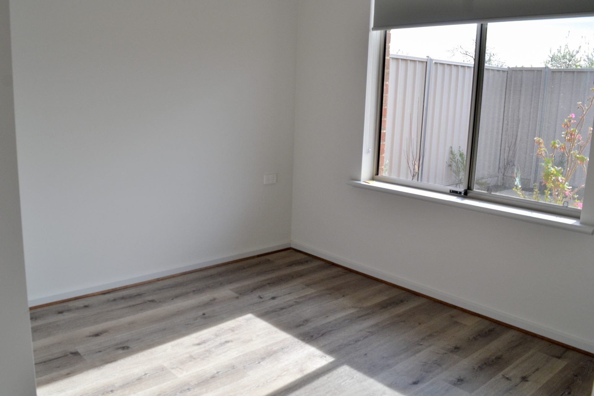 Empty bedroom with timber flooring. Window overlooks rear yard with native plant life. 