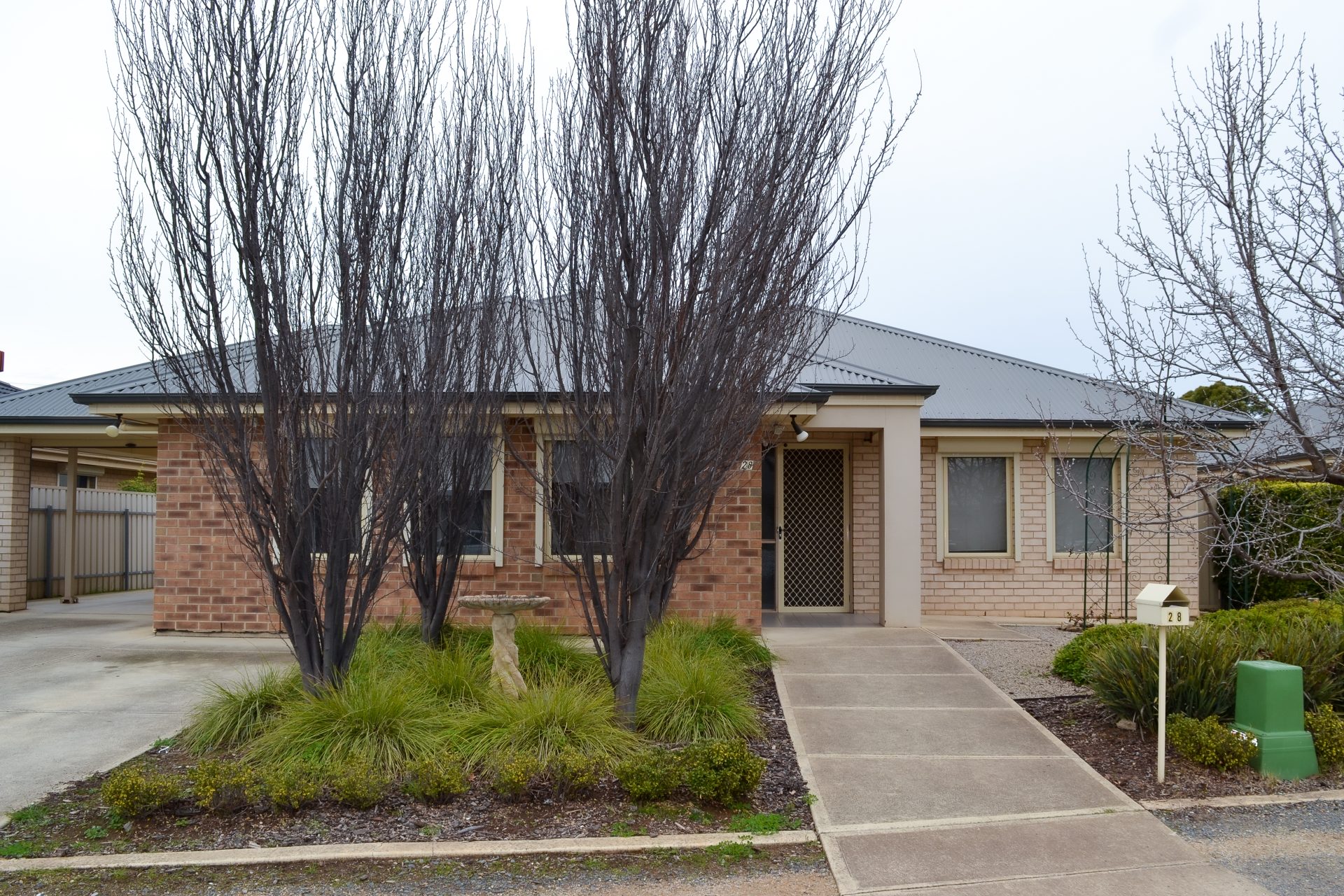 Morphetteville home 1, external front facade. Brown and yellow bricks with a grey tin roof. Tree lined driveway and footpath. 