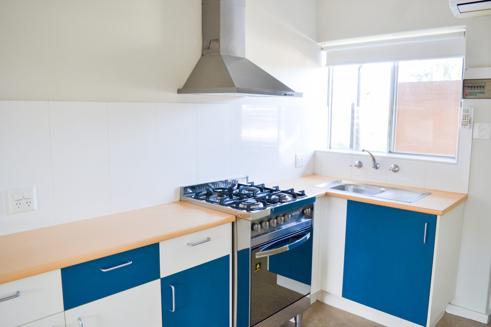 Small single bedroom apartment kitchen. White and blue cabinetry and new chrome appliances. 